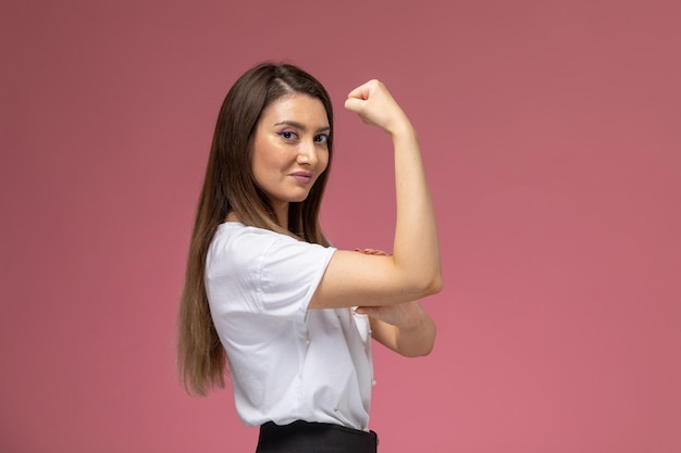 Foto gratuita vista frontal mujer joven en camisa blanca sonriendo y flexionando en la pared rosa, mujer modelo