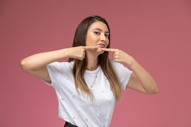 Vista frontal mujer joven con camisa blanca tocando su acné en la pared rosa, modelo de pose de mujer de color