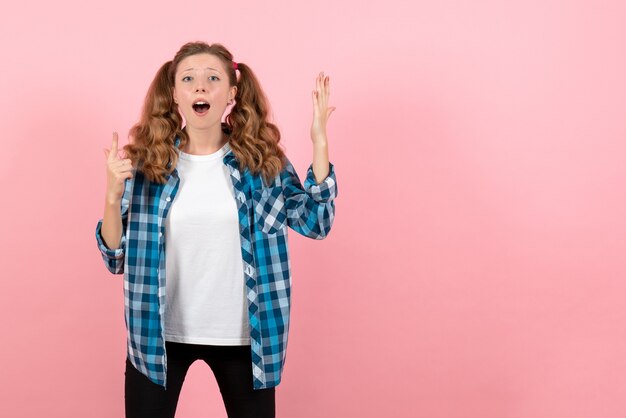 Vista frontal mujer joven en camisa a cuadros azul posando sobre fondo rosa joven emoción niña modelo moda niño