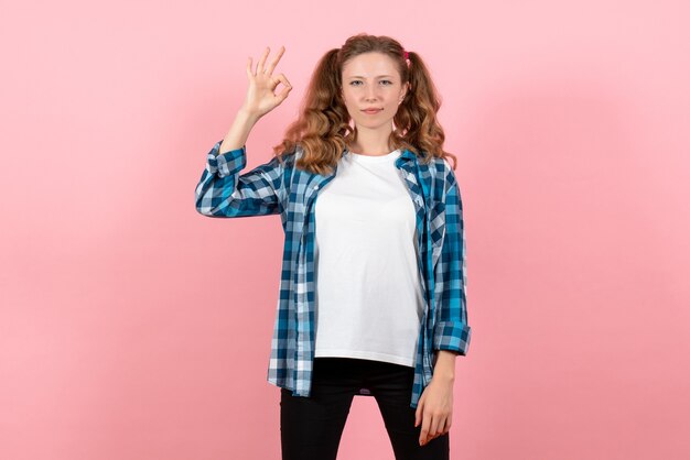 Vista frontal mujer joven en camisa a cuadros posando en escritorio rosa joven mujer emociones modelo color de niño