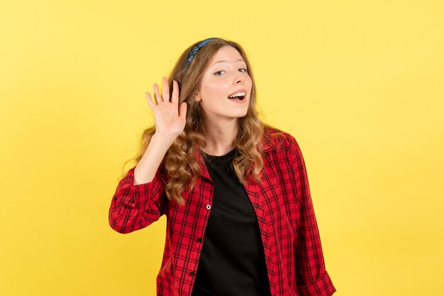 Vista frontal mujer joven en camisa a cuadros roja escuchando atentamente algo sobre fondo amarillo mujer emoción humana modelo moda chica