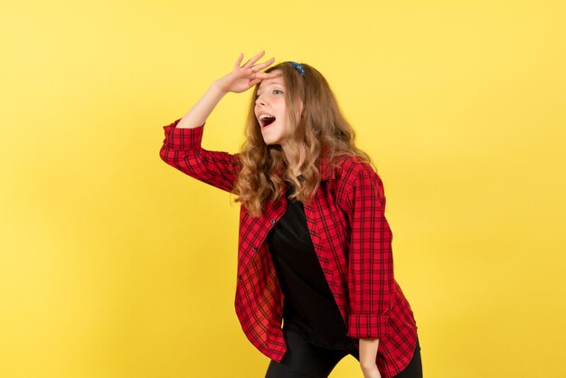 Vista frontal mujer joven en camisa a cuadros roja mirando a distancia sobre fondo amarillo mujer emociones humanas modelo moda chica