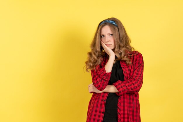 Vista frontal mujer joven en camisa a cuadros roja de pie y posando en el escritorio amarillo chica color mujer modelo humano