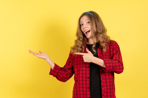 Vista frontal mujer joven en camisa a cuadros roja de pie y posando sobre fondo amarillo color mujer modelo niña humana