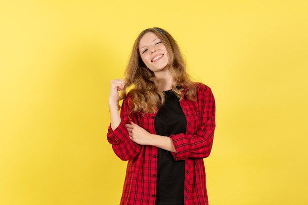 Vista frontal mujer joven en camisa a cuadros roja de pie sonriendo sobre fondo amarillo niñas modelo de color de mujer humana