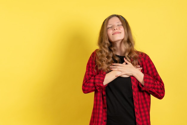 Vista frontal mujer joven en camisa a cuadros roja de pie y tocando su corazón sobre fondo amarillo niñas modelo de color humano mujer