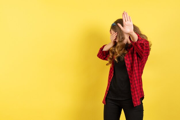 Vista frontal mujer joven en camisa a cuadros roja posando y cubriendo su rostro sobre fondo amarillo modelo niñas mujer color emociones humanas