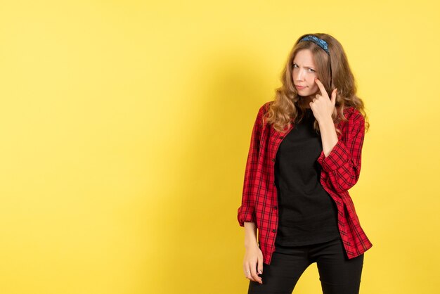 Vista frontal mujer joven en camisa a cuadros roja posando y pensando sobre fondo amarillo mujer emoción humana modelo moda chica