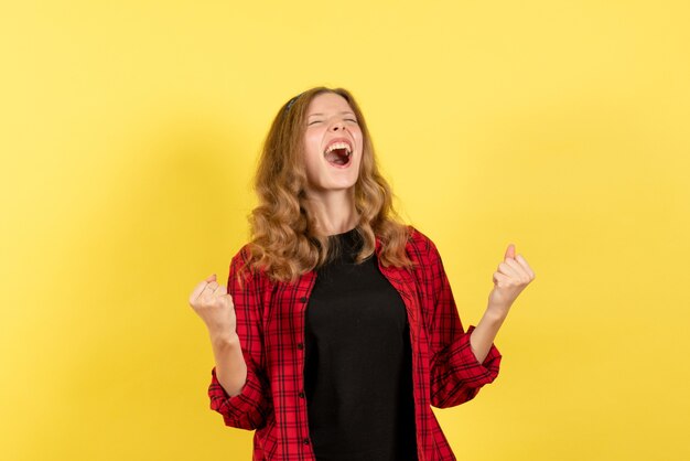 Vista frontal mujer joven en camisa a cuadros roja posando y regocijándose sobre fondo amarillo modelo de color humano mujer emoción