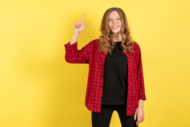 Vista frontal mujer joven en camisa a cuadros roja posando con una sonrisa sobre fondo amarillo las emociones humanas modelo de color mujer