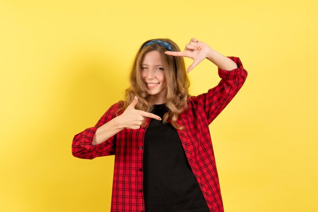 Vista frontal mujer joven en camisa a cuadros roja posando con sonrisa sobre fondo amarillo mujer emoción humana modelo moda chica