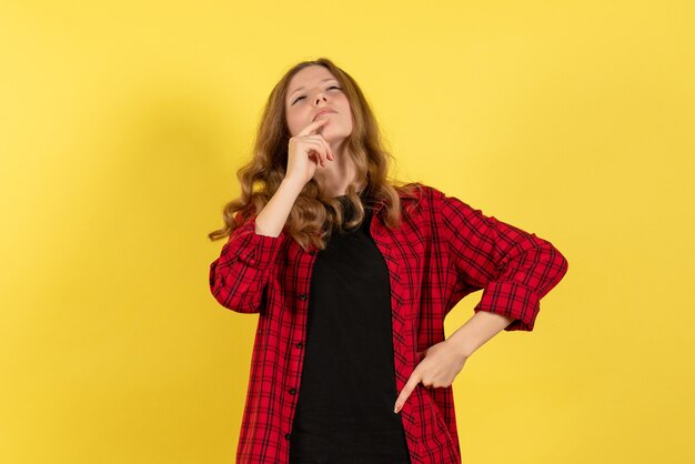 Vista frontal mujer joven en camisa a cuadros roja solo de pie y pensando en fondo amarillo modelo niñas mujer humana color emociones