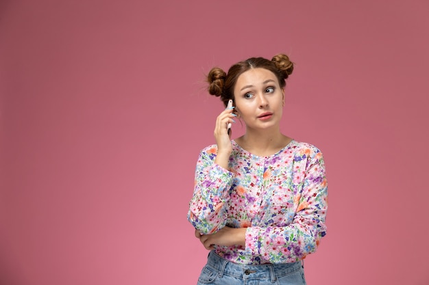 Vista frontal mujer joven en camisa de diseño floral y jeans hablando por teléfono en el fondo rosa