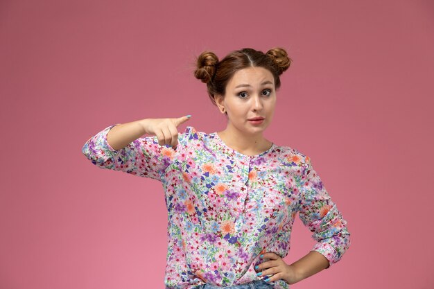 Vista frontal mujer joven en camisa de flor diseñada y jeans posando sobre el fondo rosa