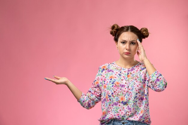 Vista frontal mujer joven en camisa de flor diseñada pensando posando sobre el fondo rosa