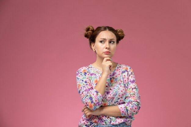 Vista frontal mujer joven en camisa de flores y jeans posign diseñado con expresión de pensamiento sobre el fondo rosa