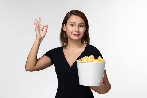 Vista frontal mujer joven en camisa negra con papas fritas posando sobre superficie blanca