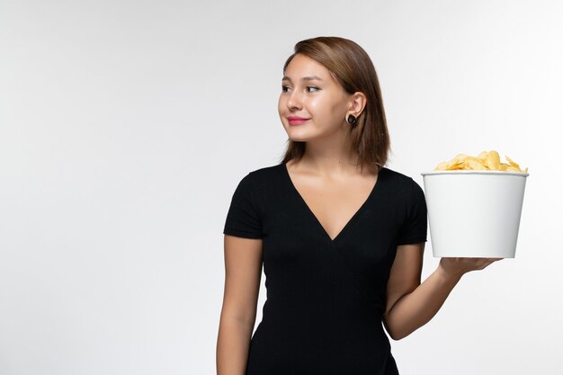 Vista frontal mujer joven en camisa negra con papas fritas en superficie blanca clara