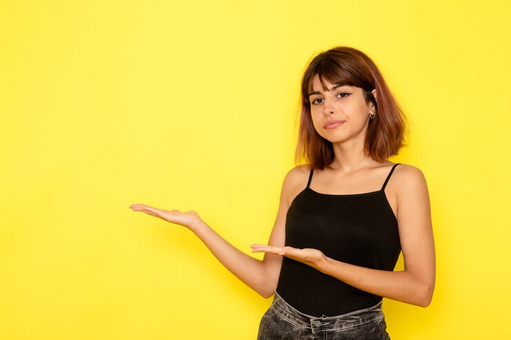 Foto gratuito vista frontal de la mujer joven en camisa negra posando en la pared de color amarillo claro