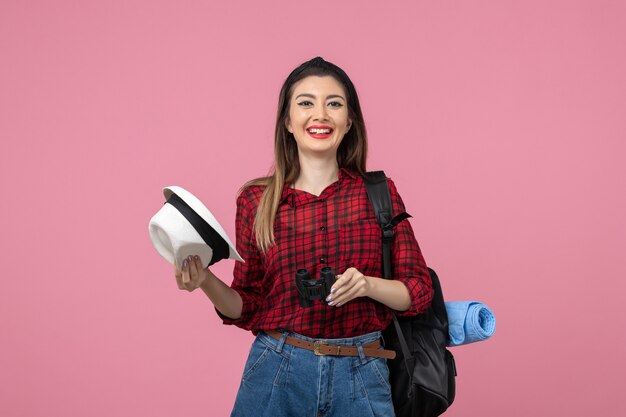 Vista frontal mujer joven en camisa roja con binoculares en el color de fondo rosa mujer humana