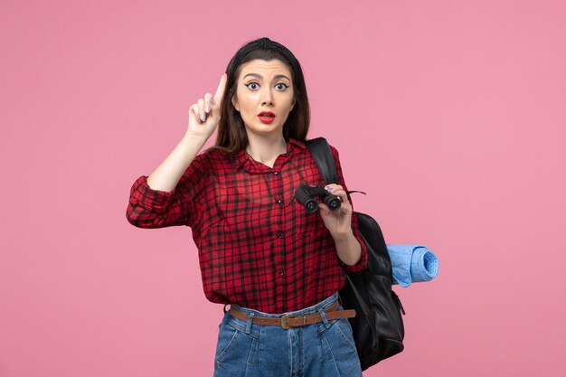 Vista frontal mujer joven en camisa roja con binoculares en color rosa estudiante mujer de escritorio