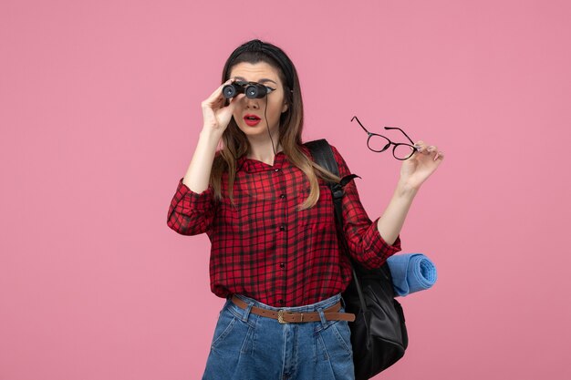 Vista frontal mujer joven en camisa roja con binoculares en modelo de foto de mujer de escritorio rosa