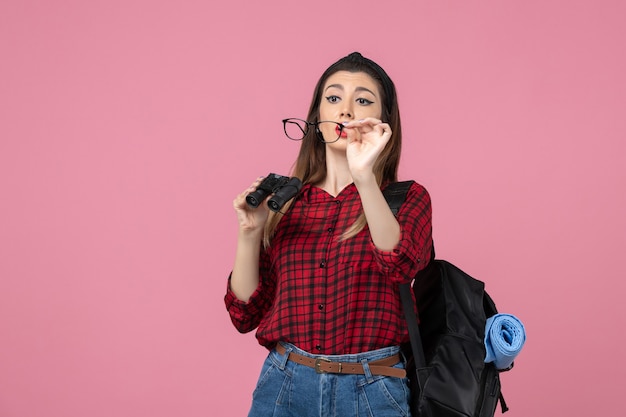 Foto gratuita vista frontal mujer joven en camisa roja con binoculares en modelo de foto de mujer de piso rosa