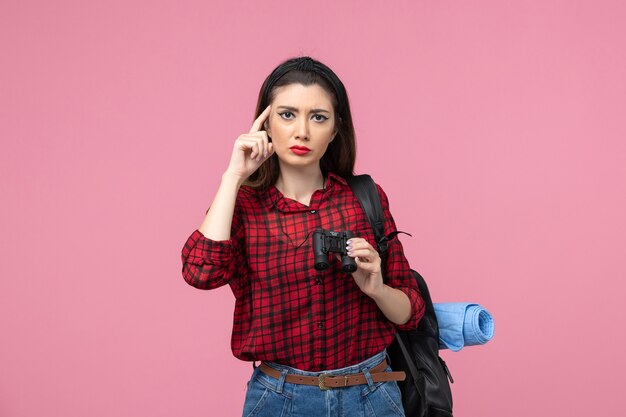 Vista frontal mujer joven en camisa roja con binoculares en la mujer de color de estudiante de fondo rosa