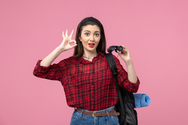 Vista frontal mujer joven en camisa roja con binoculares en la mujer de color de moda de fondo rosa