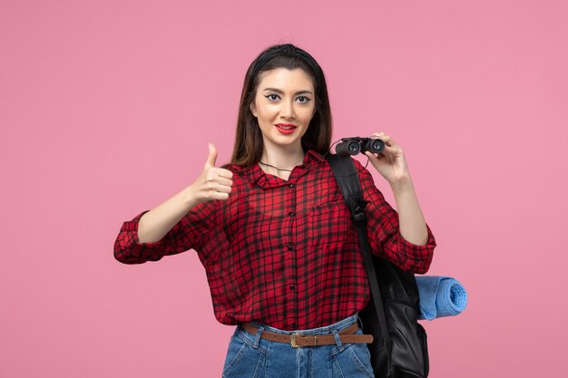 Vista frontal mujer joven en camisa roja con binoculares en la mujer de color de moda de fondo rosa