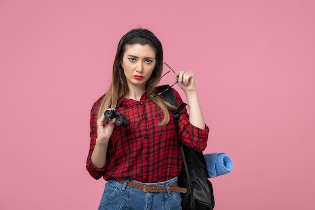 Vista frontal mujer joven en camisa roja con binoculares sobre fondo rosa claro modelo de color de mujer