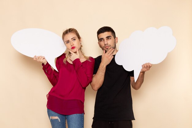 Vista frontal mujer joven en camisa roja junto con hombre sosteniendo carteles blancos en el espacio crema emoción fotográfica