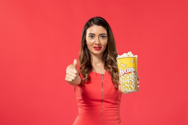 Vista frontal mujer joven en camisa roja con paquete de palomitas de maíz en la superficie roja