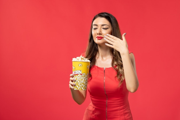 Vista frontal mujer joven en camisa roja con paquete de palomitas de maíz en la superficie roja