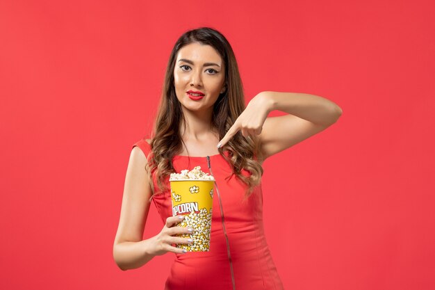 Vista frontal mujer joven en camisa roja sosteniendo palomitas de maíz en la superficie roja