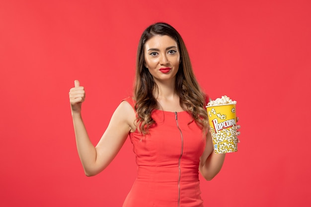 Vista frontal mujer joven en camisa roja sosteniendo palomitas de maíz en la superficie roja