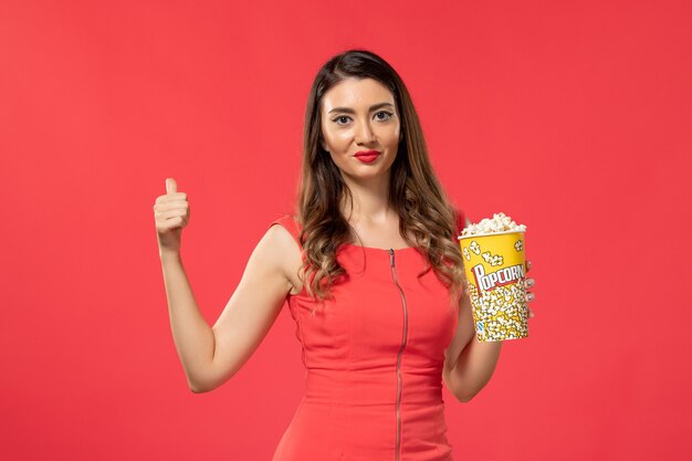 Vista frontal mujer joven en camisa roja sosteniendo palomitas de maíz en la superficie roja