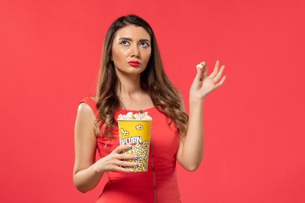 Vista frontal mujer joven en camisa roja sosteniendo palomitas de maíz en la superficie roja