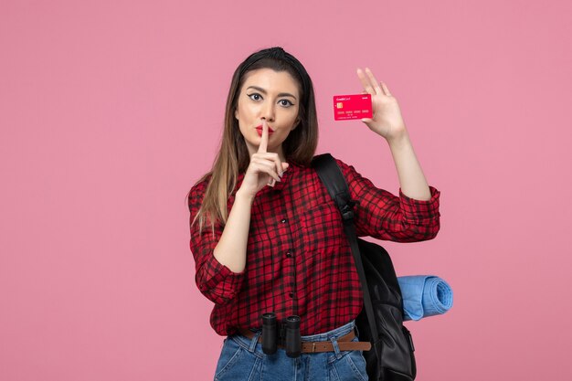 Vista frontal mujer joven en camisa roja con tarjeta bancaria en el color de la mujer humana de fondo rosa
