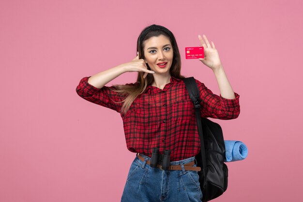 Vista frontal mujer joven en camisa roja con tarjeta bancaria en el color de la mujer humana de fondo rosa