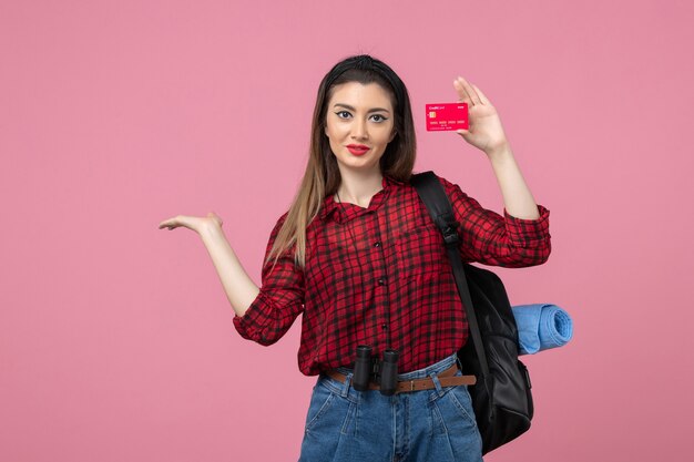 Vista frontal mujer joven en camisa roja con tarjeta bancaria en el color de la mujer humana de fondo rosa