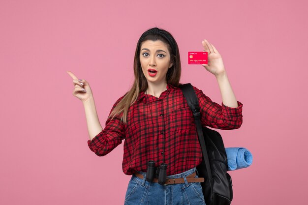 Vista frontal mujer joven en camisa roja con tarjeta bancaria en color rosa mujer humana de escritorio