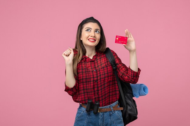 Vista frontal mujer joven en camisa roja con tarjeta bancaria en escritorio rosa mujer color humano
