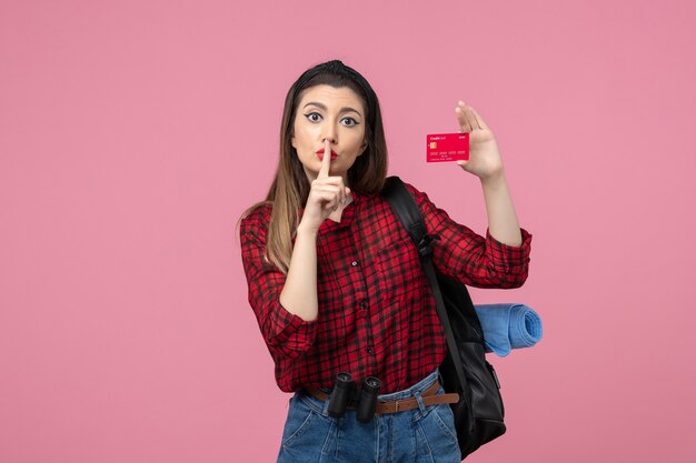 Vista frontal mujer joven en camisa roja con tarjeta bancaria en el fondo rosa mujer color humano