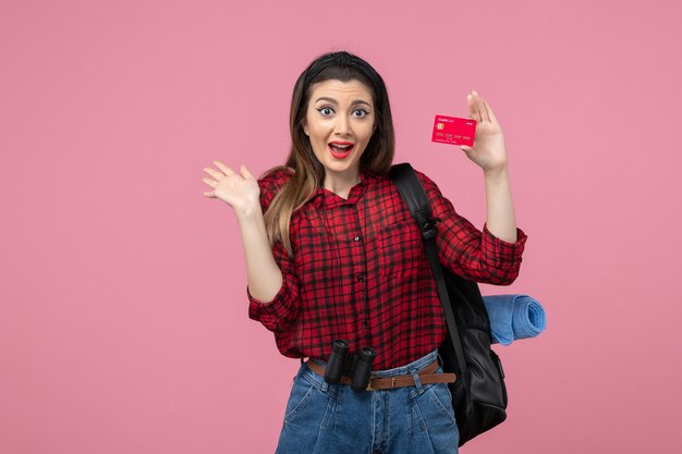 Vista frontal mujer joven en camisa roja con tarjeta bancaria en piso rosa mujer color humano