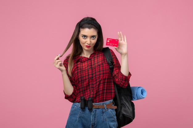 Vista frontal mujer joven en camisa roja con tarjeta bancaria sobre fondo rosa claro mujer color humano