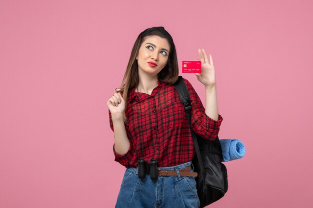 Vista frontal mujer joven en camisa roja con tarjeta bancaria sobre fondo rosa claro mujer color humano