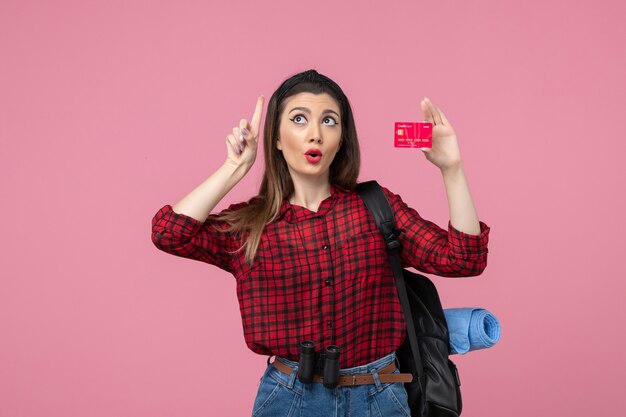 Vista frontal mujer joven en camisa roja con tarjeta bancaria sobre fondo rosa colores mujer humana