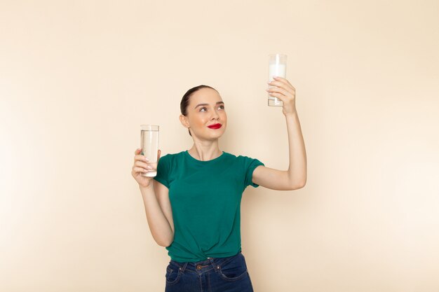 Vista frontal mujer joven en camisa verde oscuro y jeans con agua de leche sonriendo en beige