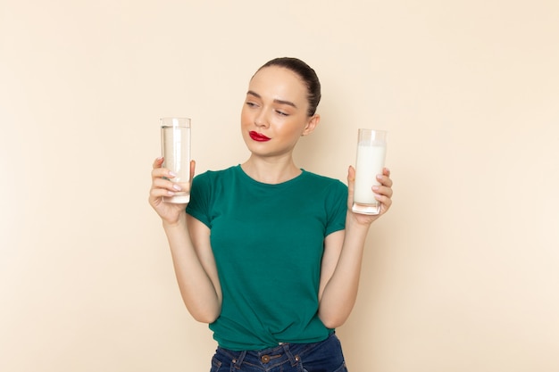 Vista frontal mujer joven en camisa verde oscuro y jeans con leche y agua en beige